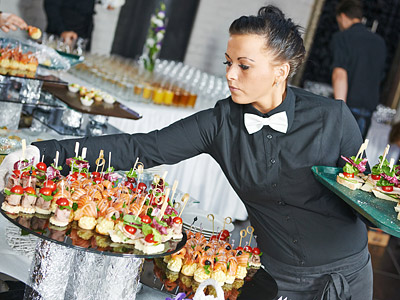 Eine Kellnerin in schwarzer Kleidung mit Fliege serviert Häppchen auf einem Fest.